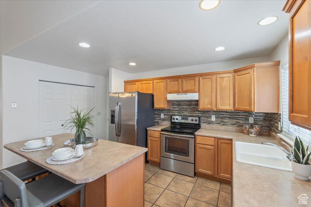 Kitchen with tasteful backsplash, light countertops, under cabinet range hood, stainless steel appliances, and a sink
