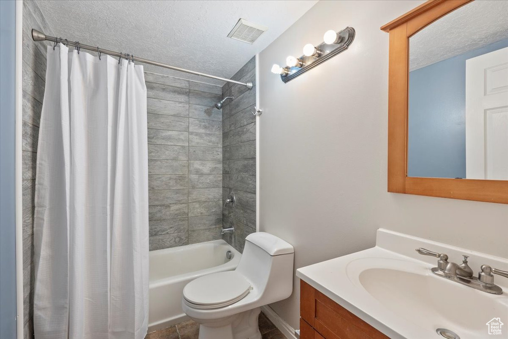 Full bathroom featuring a textured ceiling, vanity, visible vents, toilet, and shower / tub combo with curtain