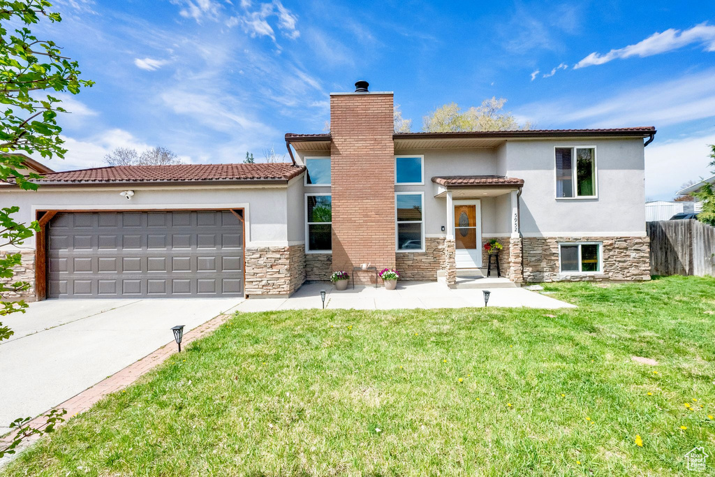 View of front of property featuring a front yard, stone siding, a garage, stucco siding, and driveway