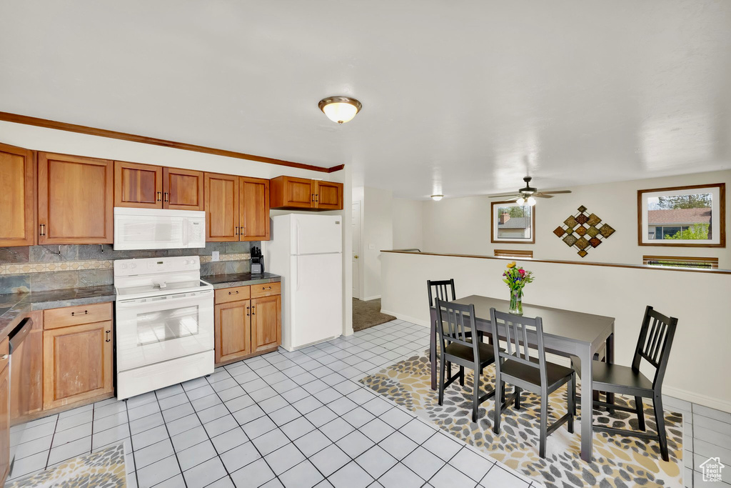 Kitchen featuring brown cabinets, light tile patterned floors, ceiling fan, and white appliances