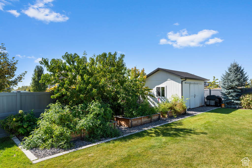 View of yard with an outdoor structure, a garden, a fenced backyard, and a storage unit