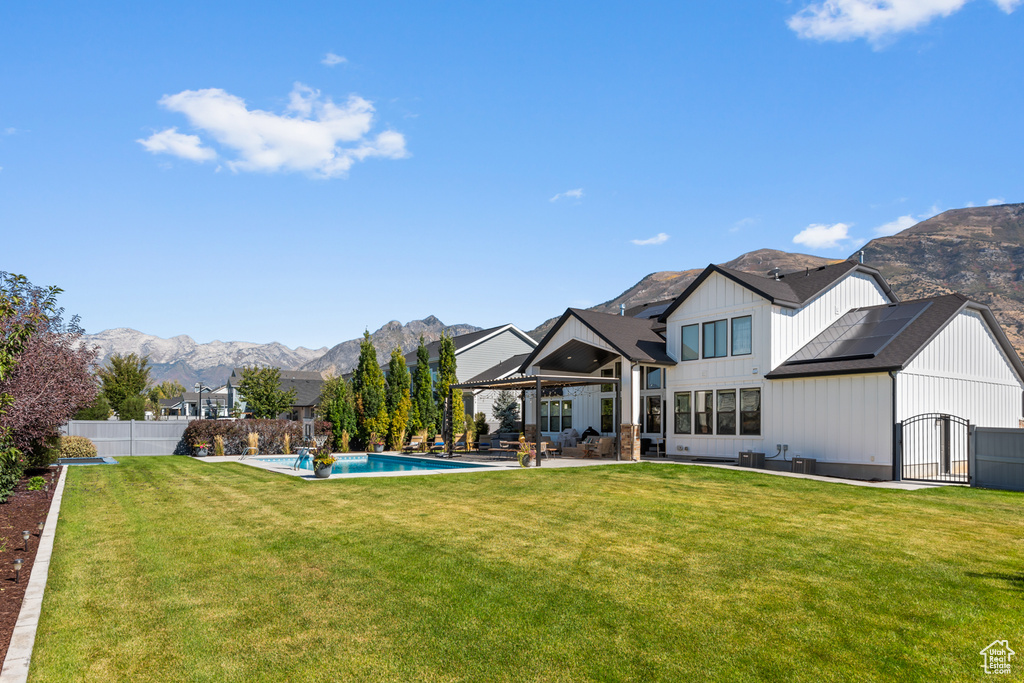 Back of house with a mountain view, a patio area, a lawn, board and batten siding, and a fenced backyard