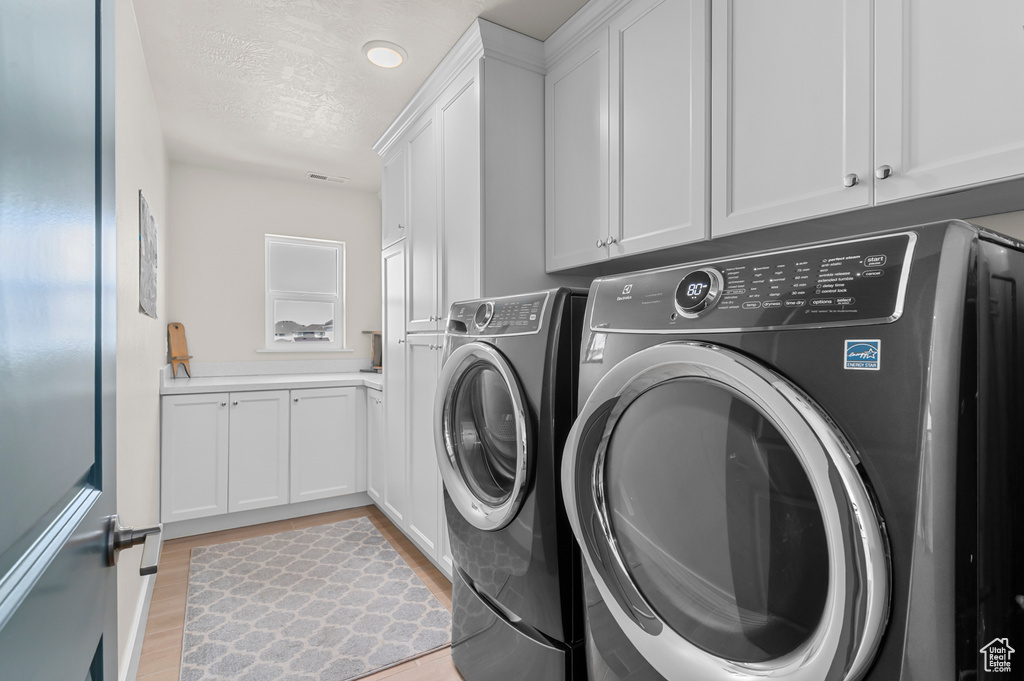 Laundry area with independent washer and dryer, a textured ceiling, light wood finished floors, and cabinet space