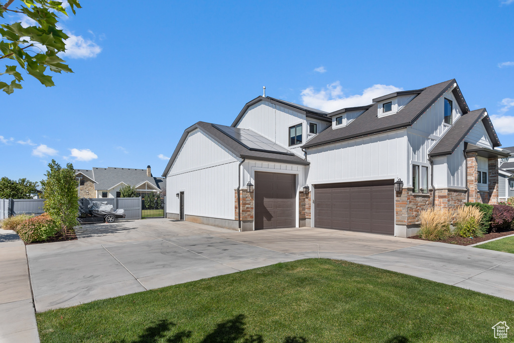 View of front of property featuring a front yard, an attached garage, stone siding, fence, and driveway
