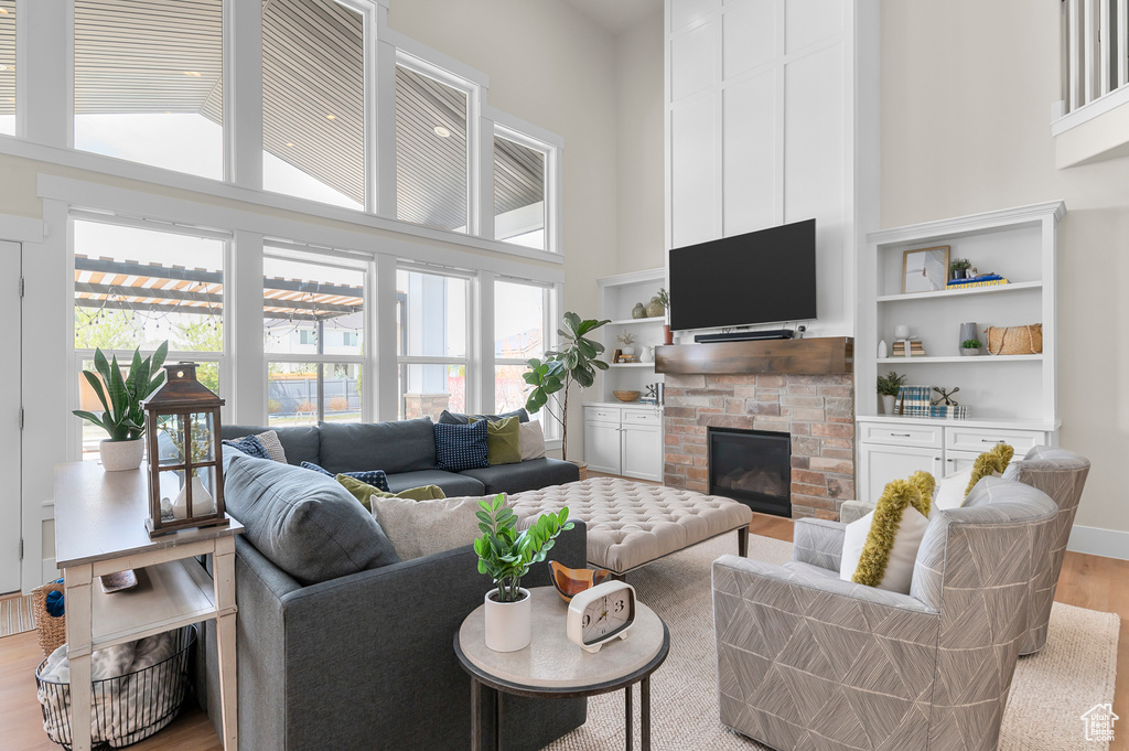 Living room with a fireplace, light wood-style flooring, and a high ceiling