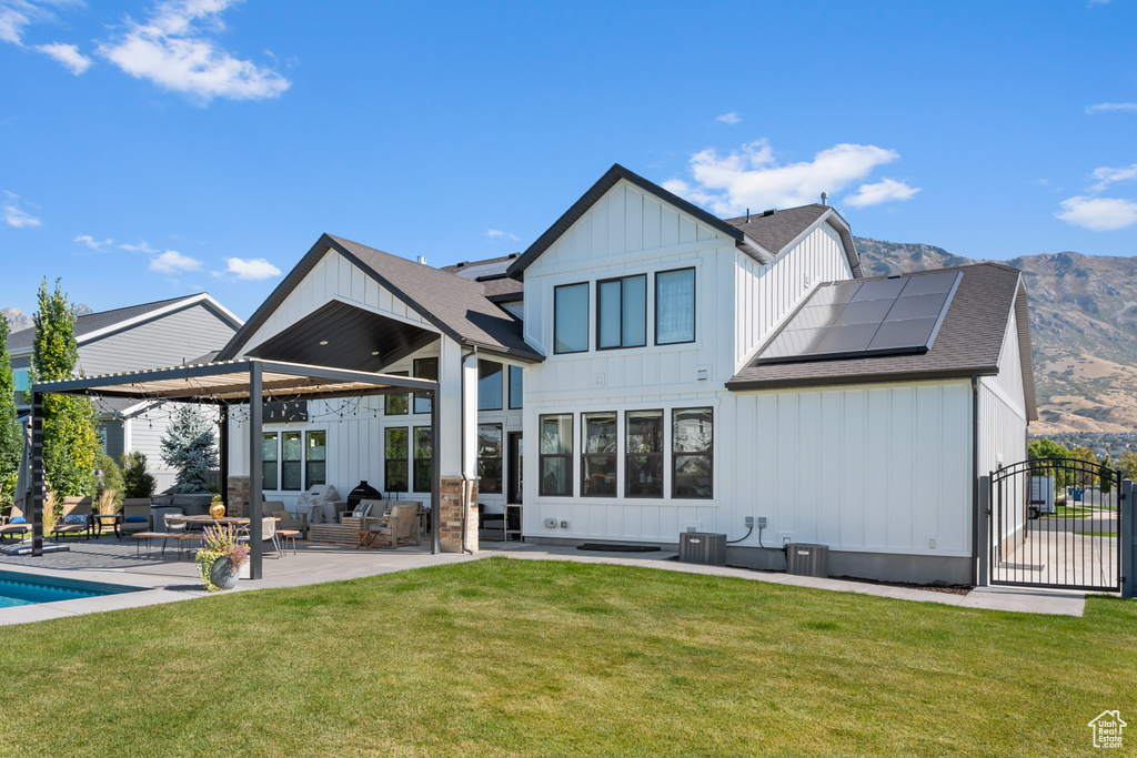 Back of property with board and batten siding, a pergola, a yard, a patio area, and solar panels