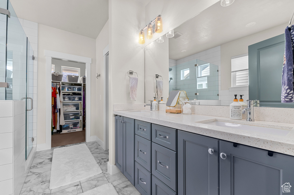 Bathroom featuring a shower stall, a spacious closet, marble finish floor, a sink, and double vanity