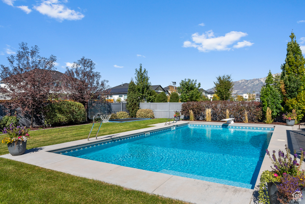 View of pool featuring a fenced in pool, a diving board, a mountain view, a fenced backyard, and a lawn