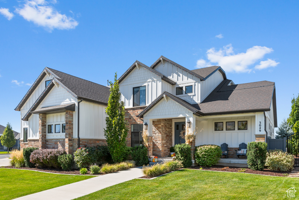 Craftsman house featuring roof with shingles, board and batten siding, a front yard, and stone siding