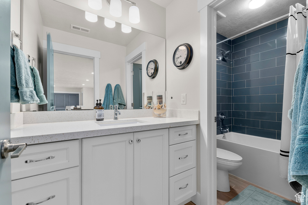 Full bathroom with visible vents, toilet, shower / bathtub combination with curtain, vanity, and wood finished floors