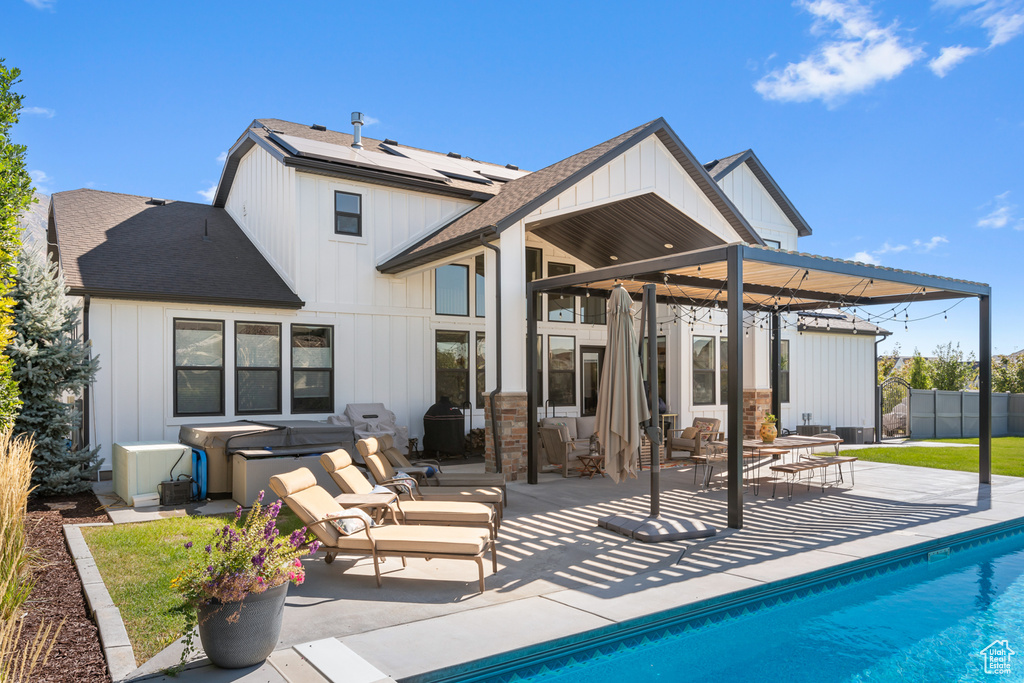 Rear view of house featuring a patio, roof with shingles, board and batten siding, a hot tub, and roof mounted solar panels