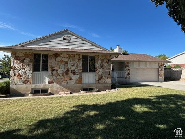 View of front of property with stone siding, an attached garage, a front lawn, concrete driveway, and a chimney