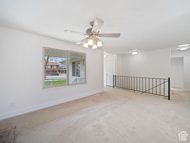 Empty room with light colored carpet, baseboards, and a ceiling fan