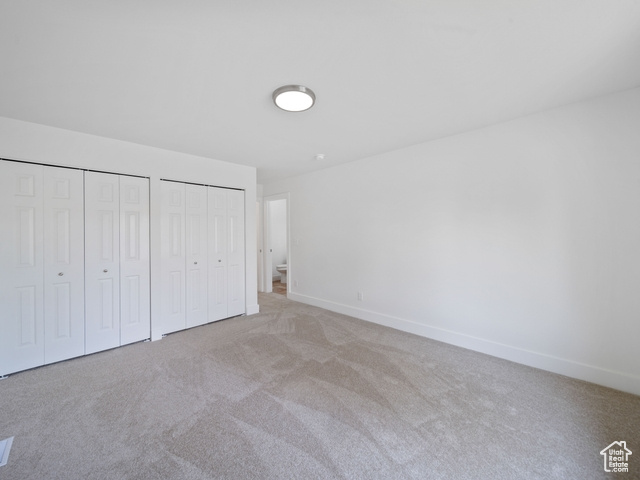 Unfurnished bedroom featuring two closets, baseboards, and light colored carpet
