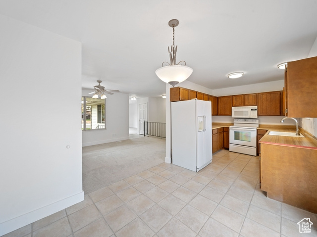 Kitchen with brown cabinetry, light countertops, white appliances, and a sink