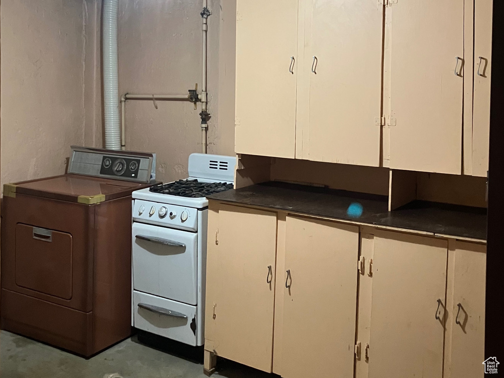 Kitchen with white gas stove, concrete flooring, white cabinets, dark countertops, and washer / dryer