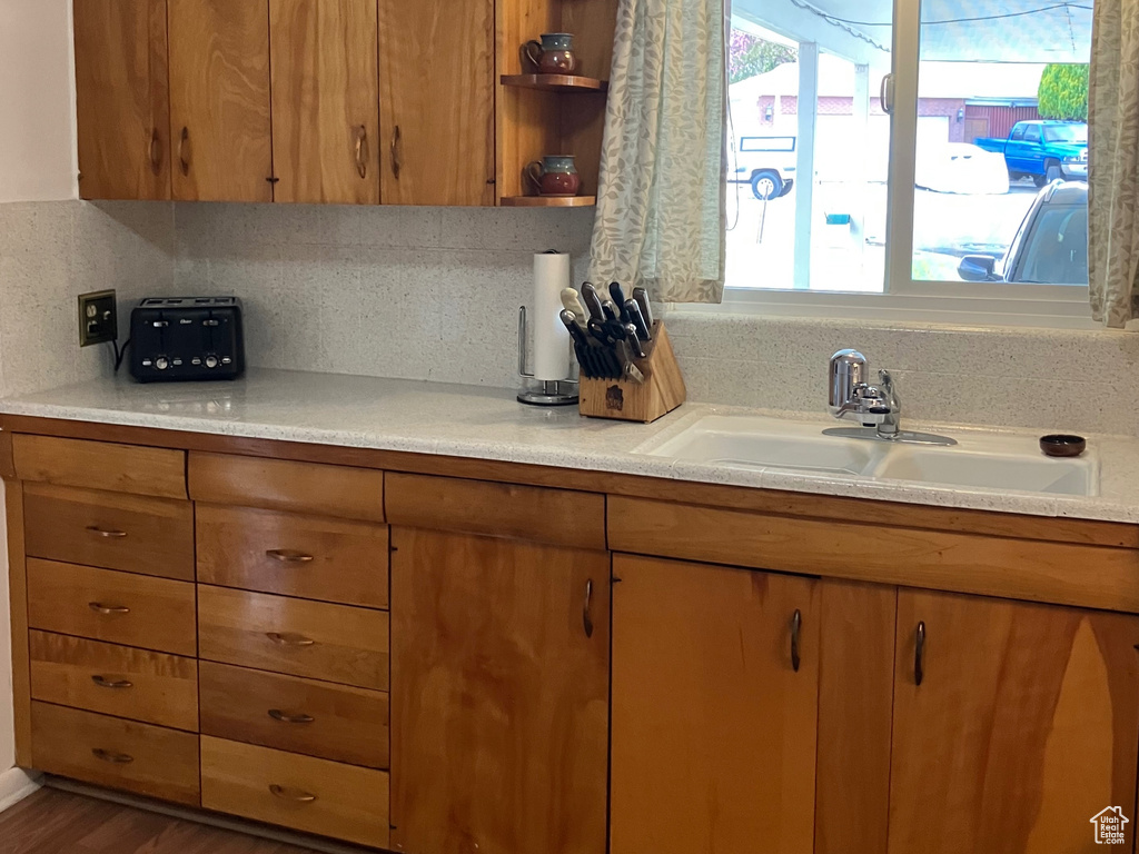 Kitchen with a sink, light countertops, brown cabinets, wood finished floors, and backsplash