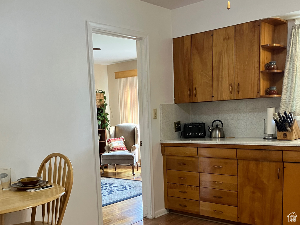 Kitchen with brown cabinetry, dark wood-style flooring, light countertops, and open shelves