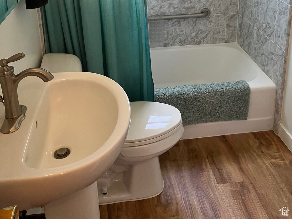 Full bathroom with toilet, wood finished floors, shower / bath combination with curtain, and a sink