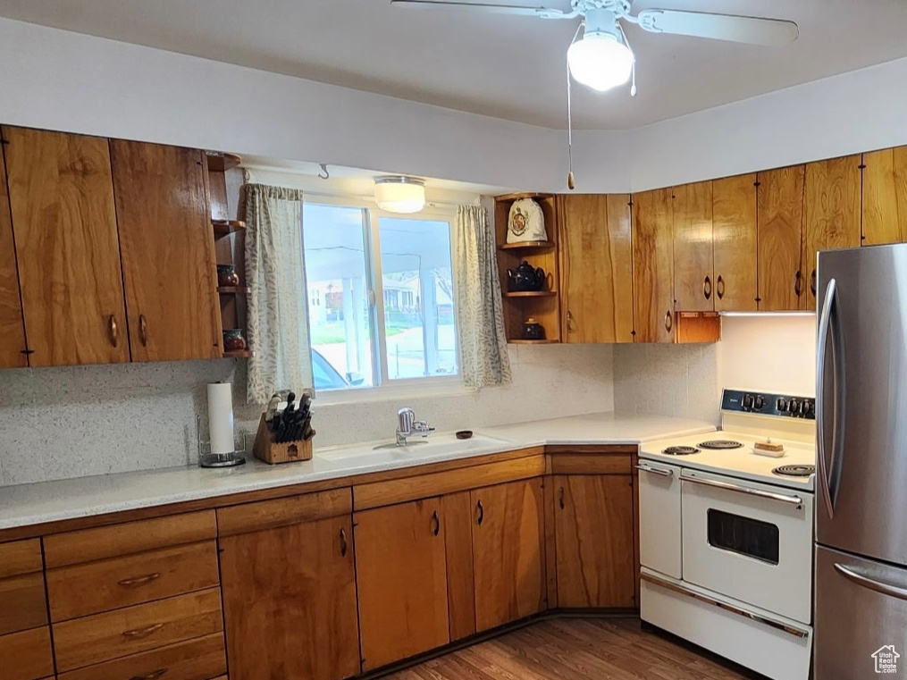 Kitchen with brown cabinetry, electric range, freestanding refrigerator, and open shelves