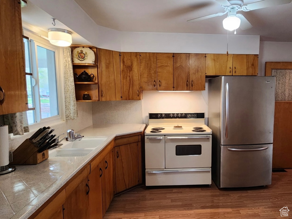 Kitchen with a sink, freestanding refrigerator, a ceiling fan, brown cabinets, and electric range