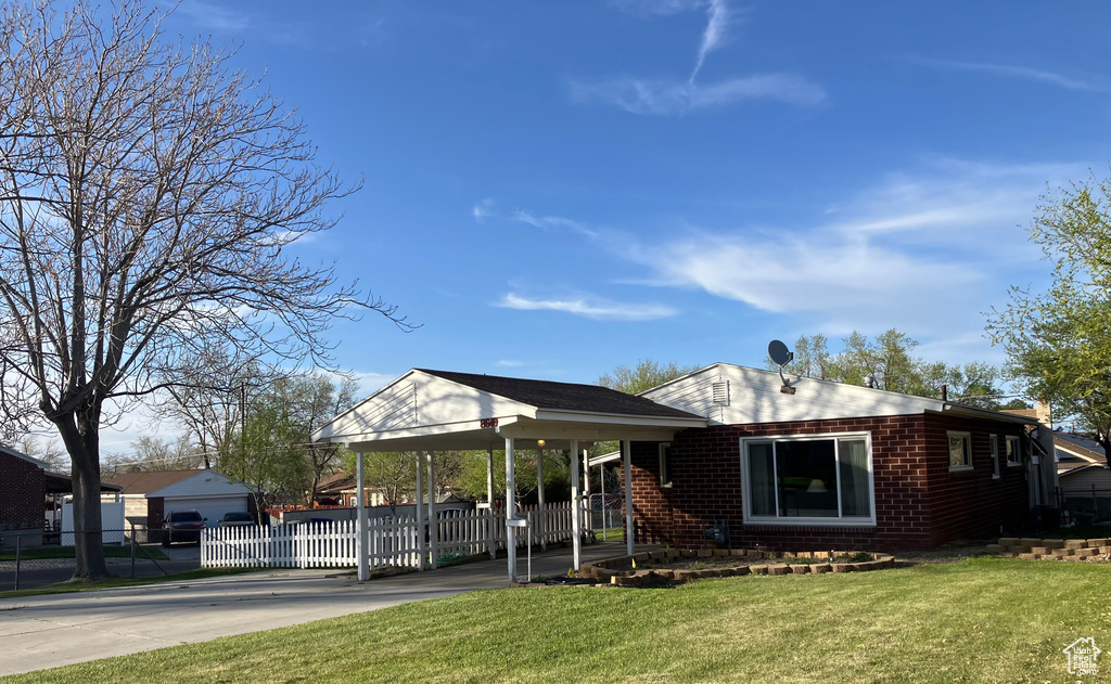 View of front of house with fence, brick siding, a front lawn, an attached carport, and driveway