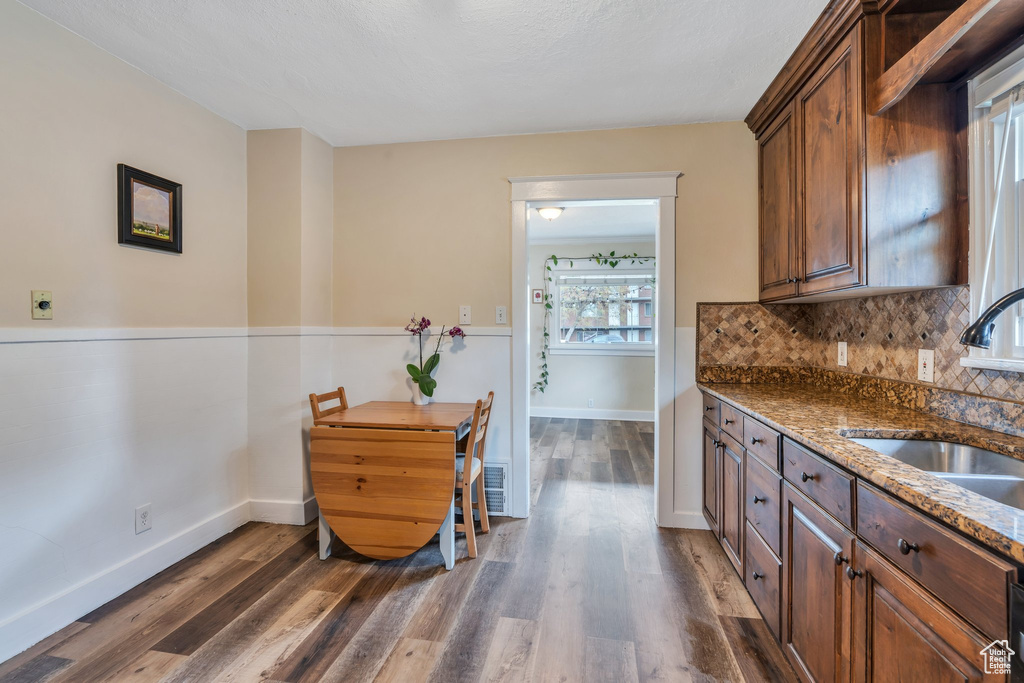 Kitchen with decorative backsplash, a sink, dark stone counters, and dark wood finished floors