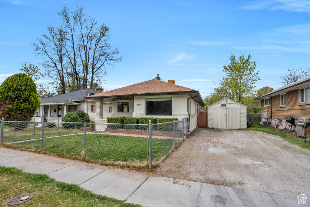 Bungalow-style home with a shed, a fenced front yard, a chimney, a front lawn, and an outbuilding