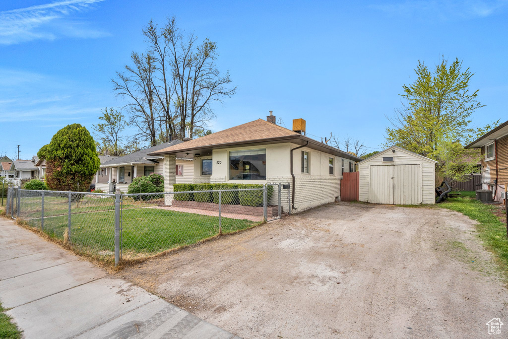 Bungalow-style house with a shed, a fenced front yard, a chimney, an outbuilding, and brick siding