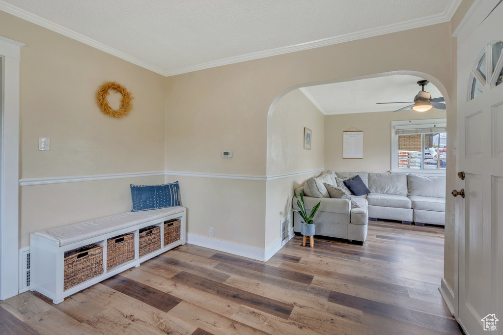 Living room with crown molding, wood finished floors, ceiling fan, arched walkways, and baseboards