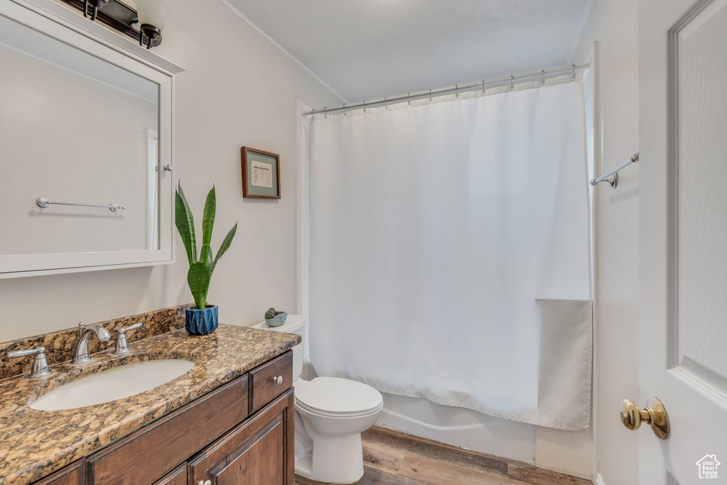 Bathroom with toilet, vanity, wood finished floors, and shower / bathtub combination with curtain
