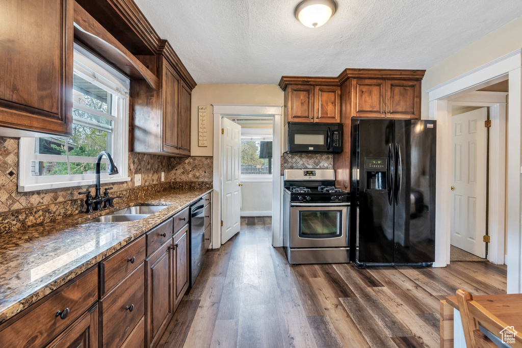 Kitchen with dark stone counters, black appliances, a sink, and dark wood-type flooring