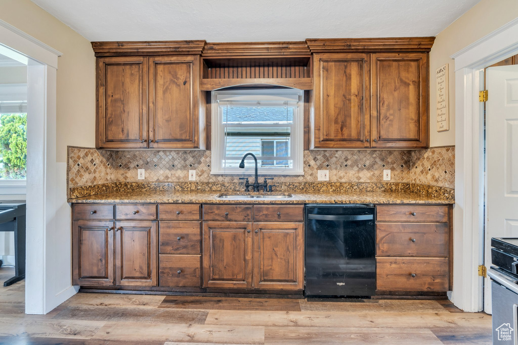Kitchen featuring dark stone countertops, a sink, light wood-style floors, decorative backsplash, and black dishwasher