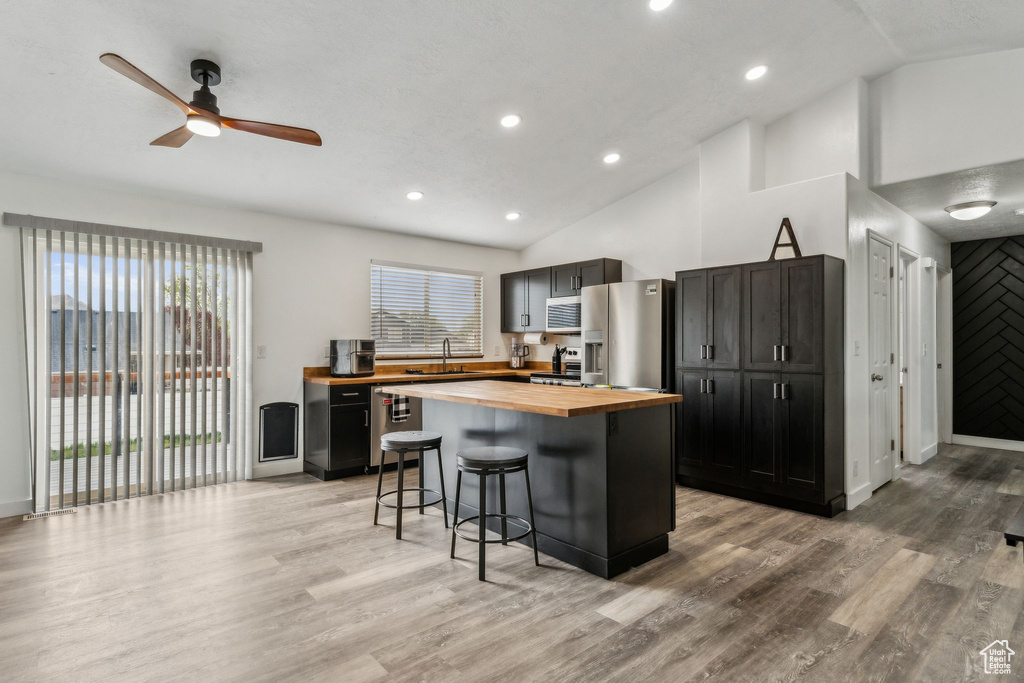 Kitchen featuring a sink, wood counters, ceiling fan, a kitchen bar, and appliances with stainless steel finishes