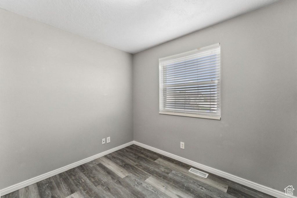 Unfurnished room with visible vents, baseboards, and dark wood-type flooring