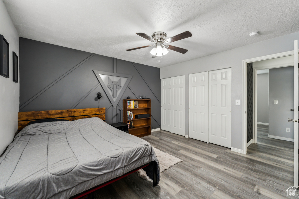 Bedroom featuring wood finished floors, a textured ceiling, multiple closets, ceiling fan, and baseboards