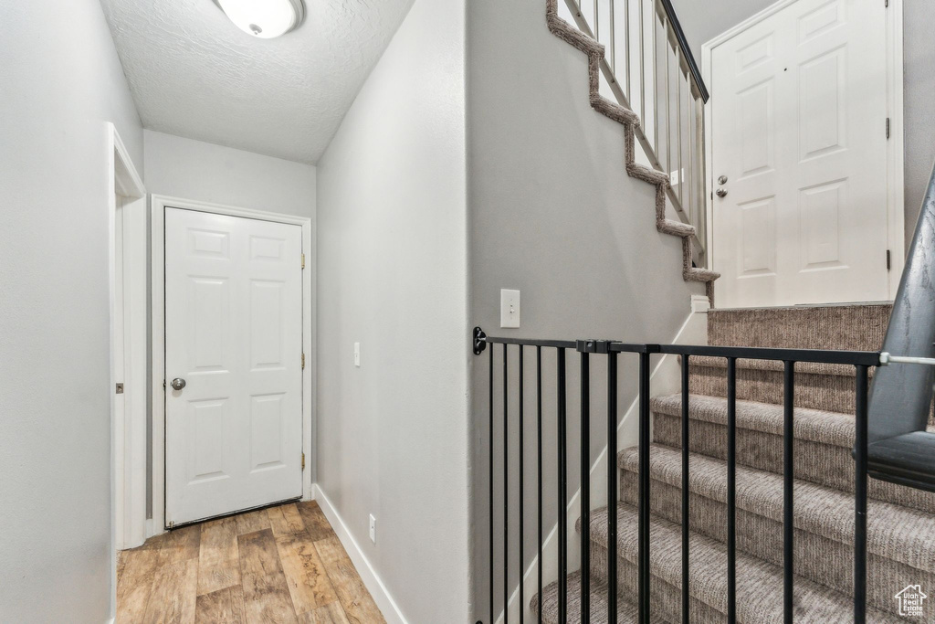 Hallway featuring light wood-style flooring, a textured ceiling, baseboards, and stairway