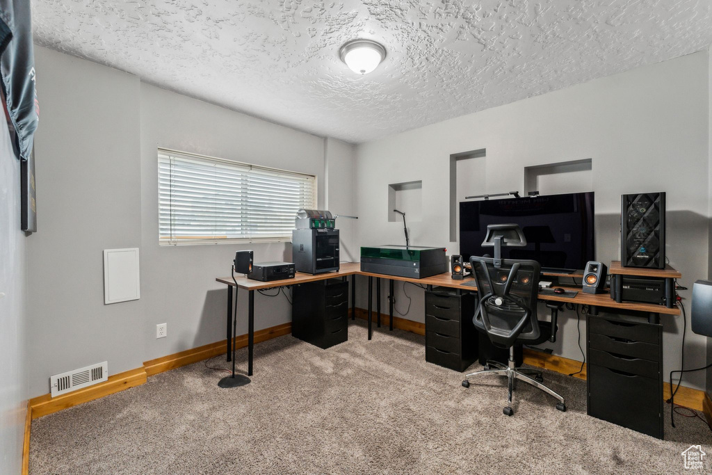 Carpeted home office featuring baseboards, visible vents, and a textured ceiling