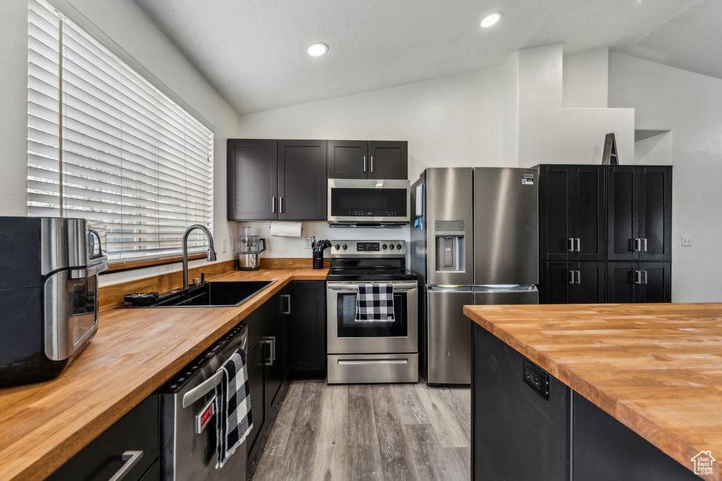 Kitchen featuring lofted ceiling, light wood finished floors, wooden counters, a sink, and appliances with stainless steel finishes