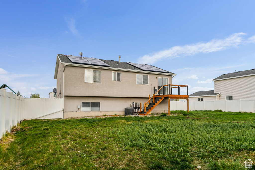Back of property featuring a fenced backyard, stairway, a deck, roof mounted solar panels, and stucco siding