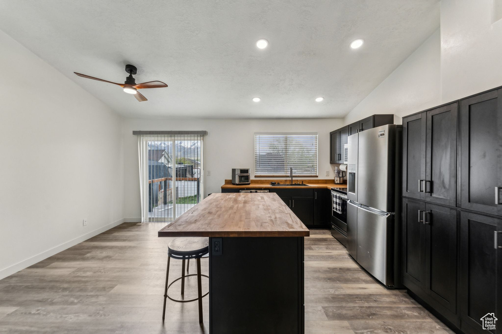 Kitchen featuring vaulted ceiling, a kitchen breakfast bar, butcher block countertops, stainless steel fridge with ice dispenser, and a kitchen island