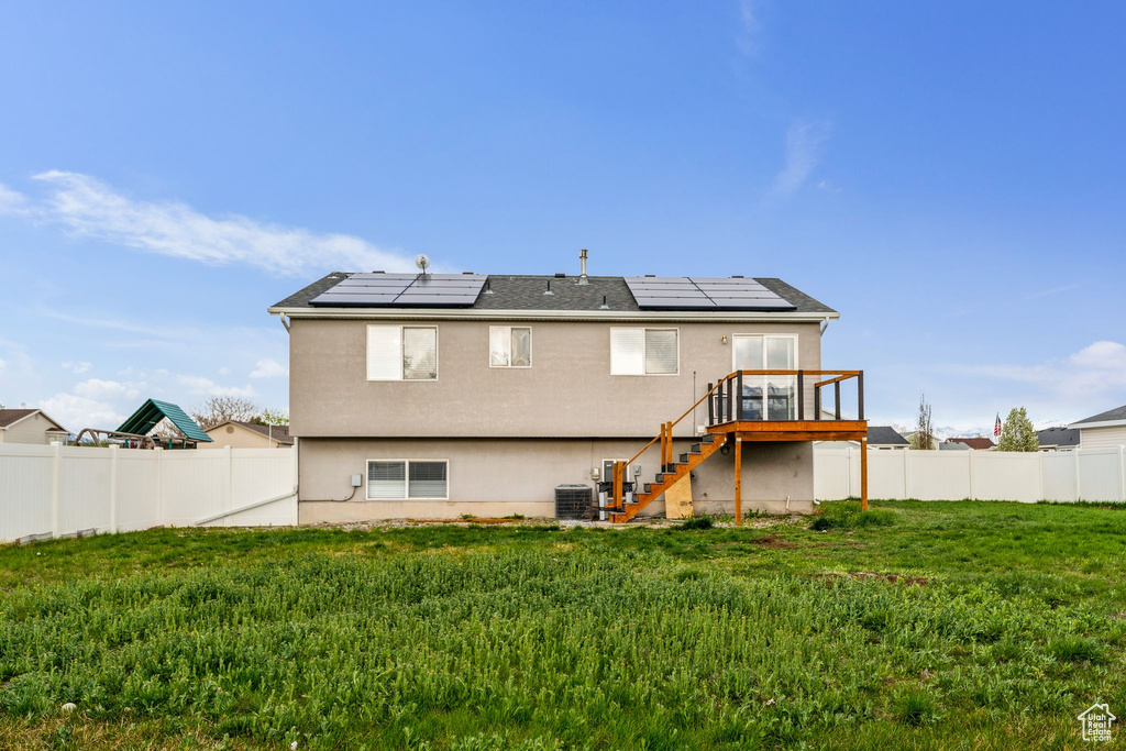 Rear view of property with a fenced backyard, solar panels, a wooden deck, a lawn, and stairway