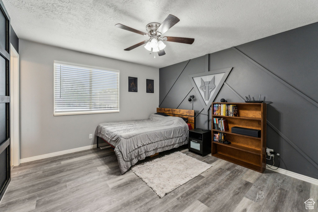 Bedroom featuring baseboards, a ceiling fan, wood finished floors, and a textured ceiling