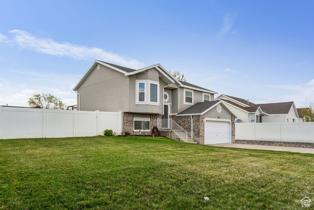 View of front of house featuring a front lawn, driveway, fence, brick siding, and stucco siding
