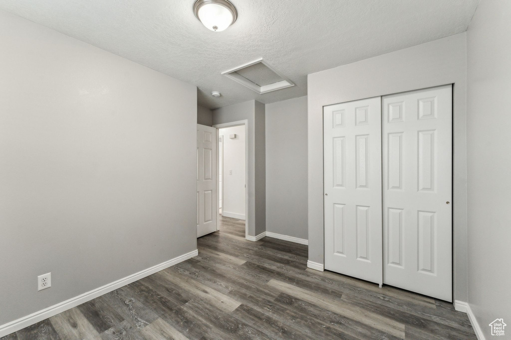 Unfurnished bedroom featuring attic access, wood finished floors, baseboards, and a closet