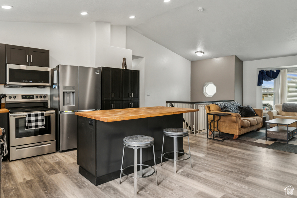 Kitchen featuring stainless steel appliances, vaulted ceiling, butcher block countertops, a kitchen island, and a breakfast bar area