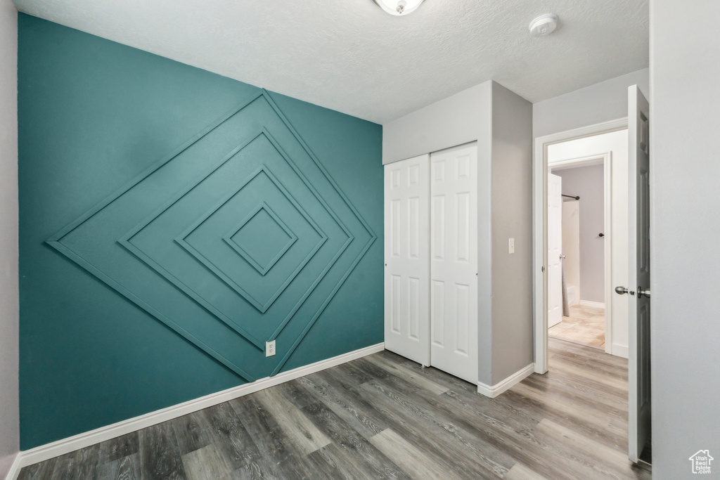 Unfurnished bedroom featuring baseboards, wood finished floors, a textured ceiling, and a closet