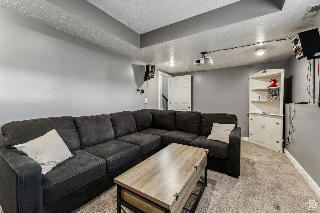 Living room featuring baseboards, visible vents, a textured ceiling, and light colored carpet