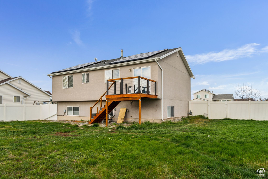Back of house with roof mounted solar panels, a fenced backyard, stairway, and a deck