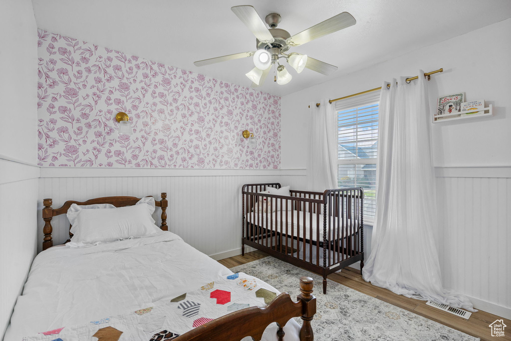Bedroom with wood finished floors, visible vents, a wainscoted wall, and ceiling fan